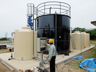 発酵槽（中央のタンク）と調整槽（左）、液肥用タンク（右）、制御盤（手前）などを備えるメタン発酵試験用プラント＝23日午後、石垣市し尿処理場内