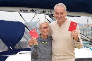 スイスのパスポートを手に「シャマド」号の前に立つマーク・デコッレさん（右）とシルヴィ・コーエンさん＝16日午後、浜崎町のヨットハーバー