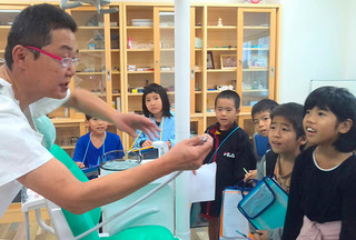 波照間歯科診療所を訪れ、歯科医の坂口克幸氏（左）から説明を受ける波照間小中学校の小学２年生たち＝21日、同診療所