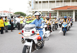 白バイを先頭に車両パレードに向かう警察官や市民ボランティアら＝21日夕、八重山警察署玄関前