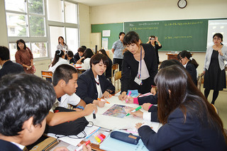 カンボジアに派遣された八重山商工高校の大城美由紀教諭（正面）の説明を受けながら、写真のタイトルを考える生徒たち＝６日午後、同校