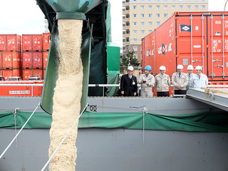 石垣島製糖や船会社の関係者が見守る中、運搬船に積み込まれていく粗糖＝26日午前、石垣港