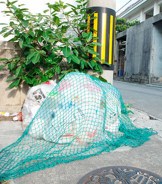 門前に出された「もやすごみ」。猫やカラスに荒らされないようネットをかぶせている＝15日午前、石垣市内