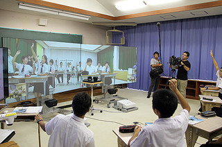 大型スクリーンを搭載したＩＣＴ（情報通信技術）機器で授業を受ける与那国中（スクリーン上）と久部良中の生徒ら＝14日午後、久部良中