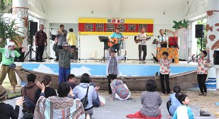 悪天候の中、第21回鳩間島音楽祭に集まった人たち。ゆったりと舞台の音楽を楽しんだ＝３日午後、鳩間島公民館前野外ステージ