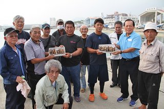 会員からエギ贈呈を受けた新入会員の浜さん（中央左）、川満さん（同右）＝５日午後、石垣漁港