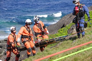 崖の下から負傷者を運ぶ消防隊員ら＝29日、崎枝御神埼灯台周辺