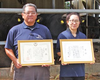 賞状を手に笑顔の上江洲さん（左）と嶺岸さん＝10月31日午前、農業生産法人㈲ヤイマ・ブリーダー・ランチ牛舎前