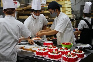 クリスマスに向けてデコレーションケーキの飾りつけを行うスタッフ＝24日午前、メームイ製菓本店