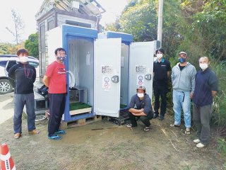 仮設型のバイオトイレを2基設置。事業を運営する関係者ら＝20日午後、西表島マーレー駐車場