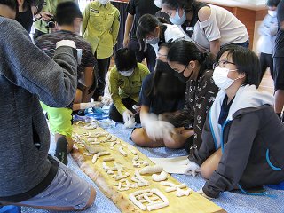 自分たちでデザインした文字や図柄の看板をサンゴ礫を貼り付けて作る児童ら＝5日午後、八島小学校体育館