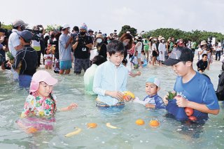 初泳ぎで果物を集める子どもたち。八重山から一足早い夏の到来を全国にアピールした＝20日午前、竹富島コンドイ浜