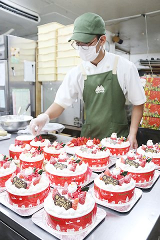 イチゴやパーツなどを飾り付けクリスマスケーキを仕上げていくスタッフ＝24日午後、メームイ製菓本店