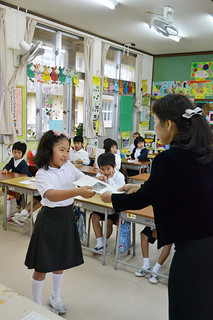宮良小学校１学年担任の浅井美枝教諭（右）から通知表を受け取る児童＝25日午前、同校