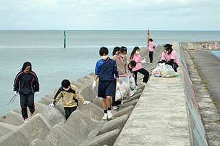 消波ブロックに捨てられたごみを拾う八重山商工高校観光コースの生徒たち＝８日午前、八島小南側の防波堤周辺