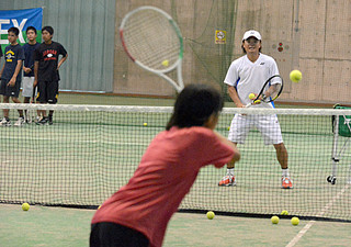 子どもたちにテニスを指導する元プロの本村剛一さん（奥）＝５日午前、市中央運動公園屋内練習場
