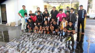 漁師の仕事を体験し、釣果を前に記念写真に収まる久部良中学校の生徒ら＝14日、与那国漁協セリ場