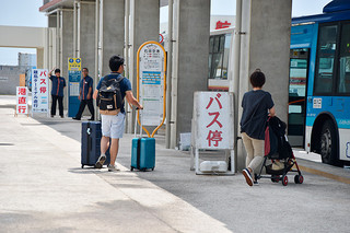 ２社が設置したバス停の看板と行き交う観光客ら＝13日午前、南ぬ島石垣空港バス乗り場