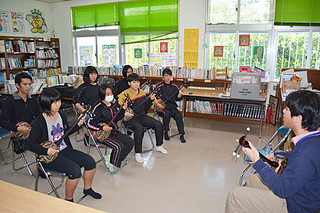 県立芸大の沢岻安優さん（右）から三線を学ぶ参加者たち＝19日午後、竹富小中