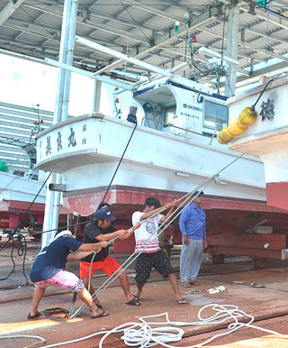 台風接近に備え、陸揚げした船をロープで固定する作業に追われる漁業関係者＝６日午前、登野城漁港