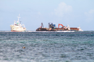 座礁した「ＳＥＰＥＨＲ」（写真左）からポンプで燃料油等を回収する台船（右）＝17日午前、川平浄化センター地先海岸