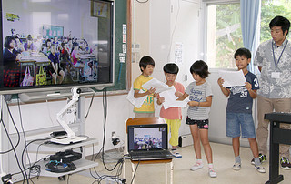 テレビ電話を通して、八重山と沖縄本島の戦争体験を紹介し合う児童ら＝20日午後、大本小学校