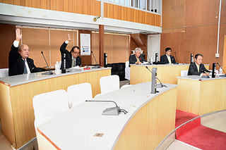 最終本会議で外間町長が提出した教育長同意の採決で挙手する与党議員（左）、賛成少数で否決となった＝15日午前、町議会