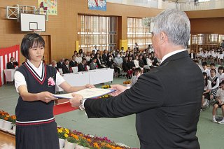 新川小学校の卒業式で、佐事安弘校長から卒業証書を受け取る卒業生（左）＝22日午前、同校体育館
