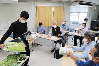 キナノキの写真を広げて説明する京都薬用植物園の坪田勝次さん（左）＝5日午後、竹富町役場仮庁舎