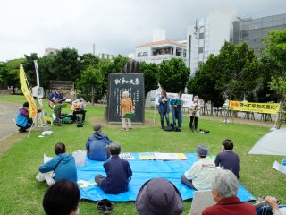 九条の碑を前に歌やスピーチで戦争放棄を訴える人たち＝3日夕、新栄公園