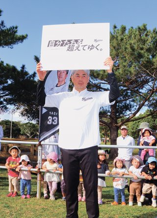 今季のチームスローガン「自分たちを超えていく。」のパネルを掲げる吉井理人監督＝1月31日午前、市中央運動公園
