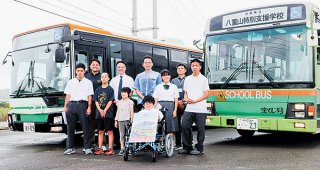 15年間使用したスクールバス（右）と新しいスクールバスの間で笑顔を見せる八重山特別支援学校の子どもたち＝18日午前、東運輸本社営業所