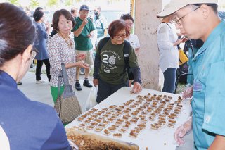 できたばかりの黒糖を試食し、笑顔を見せる来店客ら＝10日午前、ファーマーズマーケットやえやま「ゆらてぃく市場」